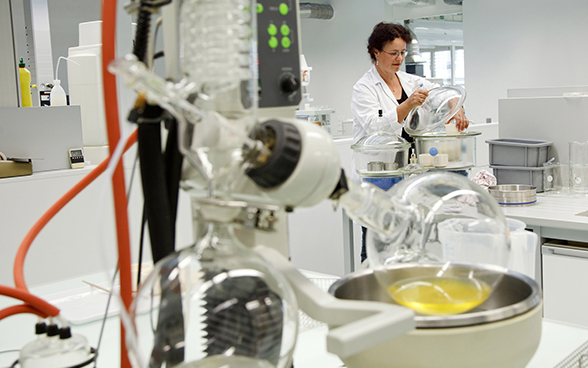 Photo représentant une laborantine, entourée de machines, en train de manipuler des flacons.