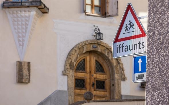 Cartello stradale in romancio che indica la presenza di una scuola nel Comune di Zuoz, Cantone dei Grigioni. 
