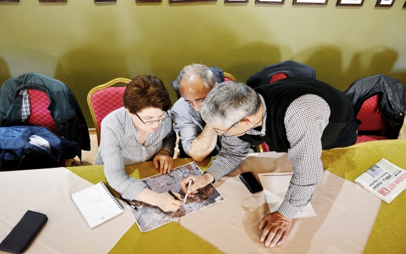 Two men and a woman bent over a map. 