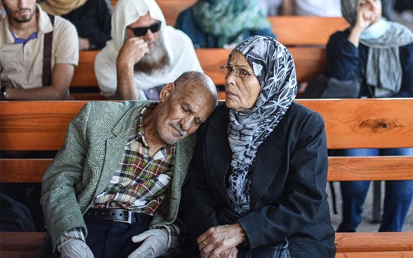 An elderly couple sits on a bench.