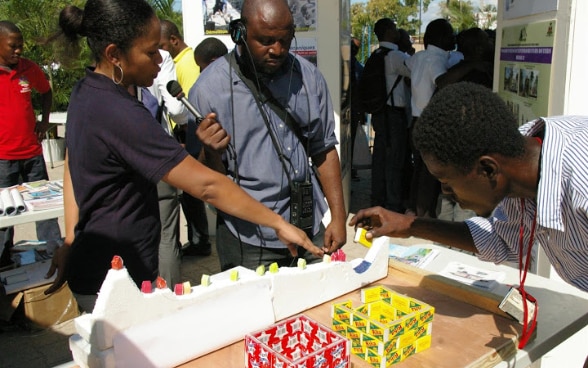 Une ingénieure haïtienne employée de la DDC répond aux questions d’un journaliste devant un stand.