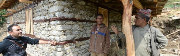 Un muratore parla con due abitanti di un villaggio davanti a un’abitazione ristrutturata.