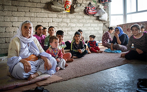 Donne e bambini seduti sul pavimento di una piccola casa ancora in costruzione in un villaggio curdo nel Nord dell’Iraq, dove sono stati reinsediati un centinaio di profughi.