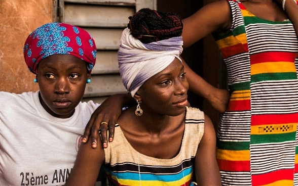 Drei farbenfroh gekleidete junge Malierinnen vor einem Haus