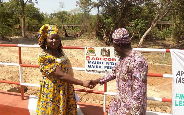 Two women on a bridge shaking hands.