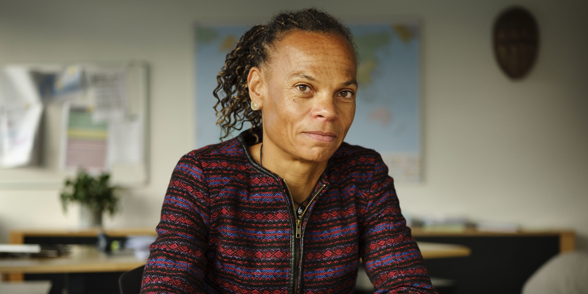 Sur la photo, la directrice de la DDC Patricia Danzi, assise à une table, fait face à la caméra. En arrière-plan apparaît son bureau avec un planisphère accroché au mur. 