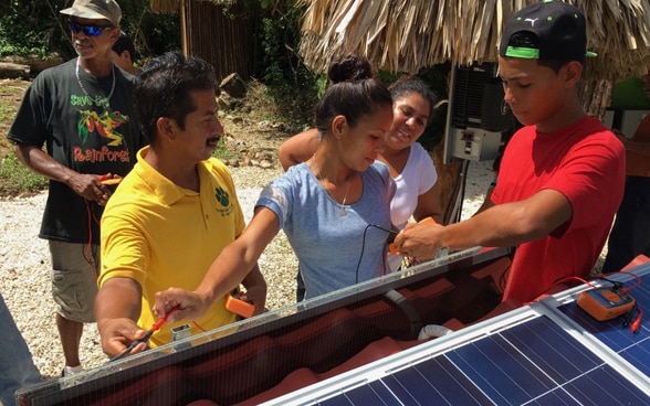  Des hommes et des femmes de la commune se tiennent devant un toit doté de panneaux solaires et reçoivent une introduction pour leur utilisation.