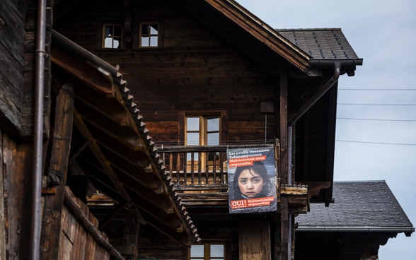 Un placard orange en faveur de l’initiative pour des multinationales responsables orne un ancien battoir de montagne, au bois noirci par le temps.