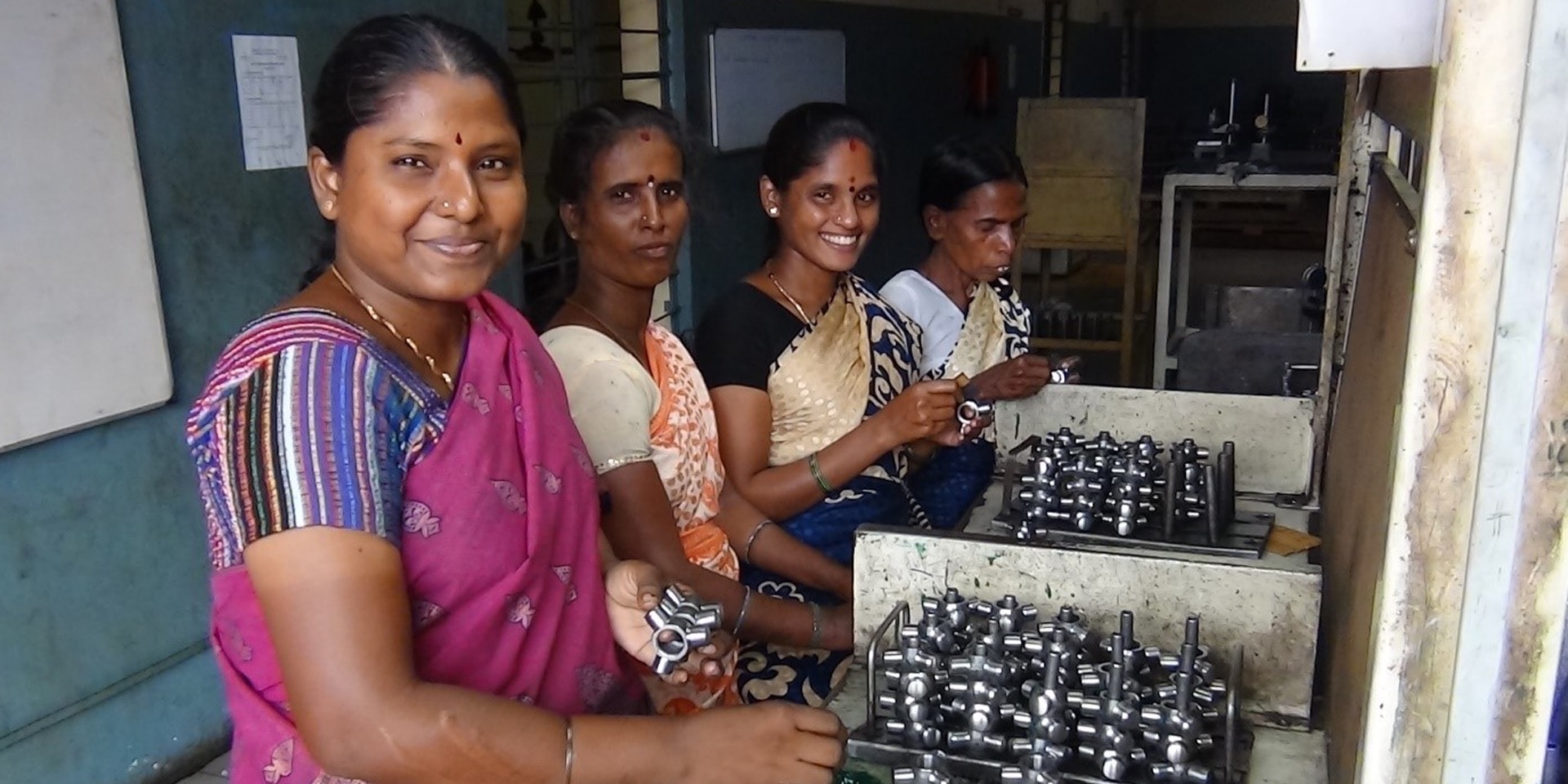En la imagen, cuatro mujeres de origen indio mientras ensamblan piezas metálicas.