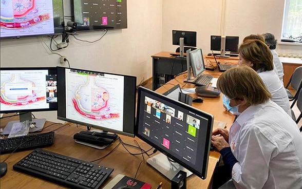Dans une salle dotée de nombreux écrans, le personnel médical travaille sur des ordinateurs.