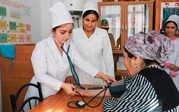 Dos médicos tayikos miden la presión arterial de un paciente sentado en una silla.