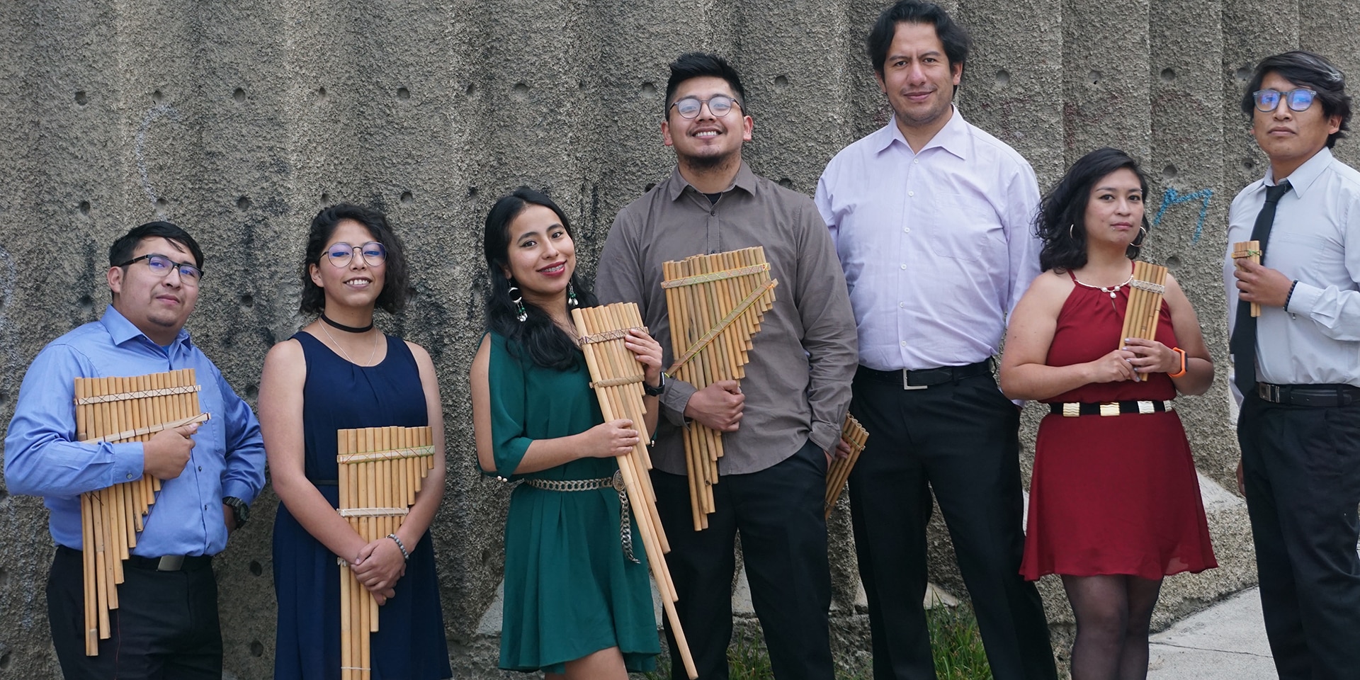 The seven musicians of the Ensemble OEIN stand next to each other. They hold pan flutes in their hands.