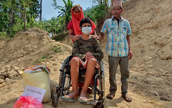 Una donna e un uomo spingono un uomo più giovane su una sedia a rotelle in Nepal.