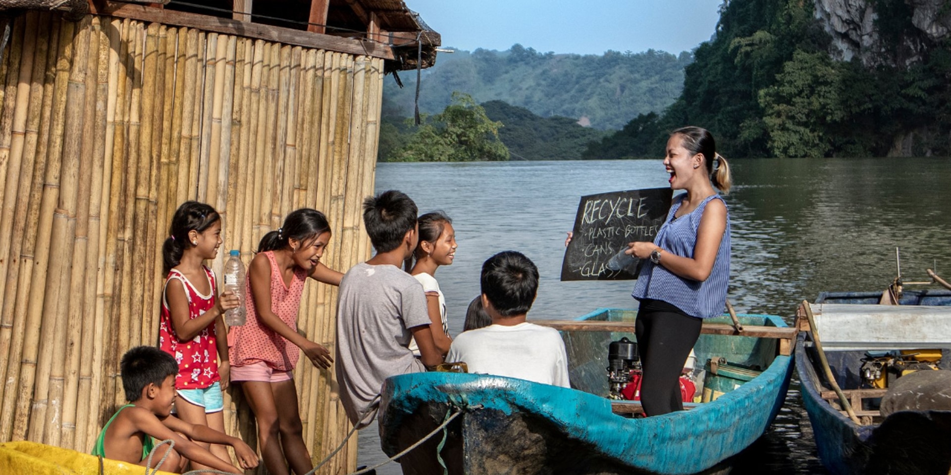 A young woman teaches children from a boat on a river in the Philippines.