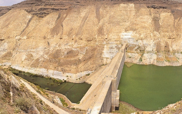 L'acqua scorre su entrambi i lati di una diga, che si trova tra due pendii montuosi.