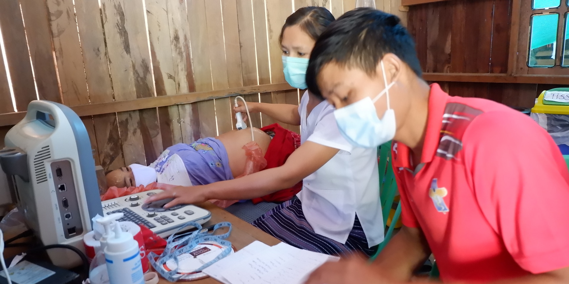 A man and a woman visit a patient and perform an ultrasound examination.