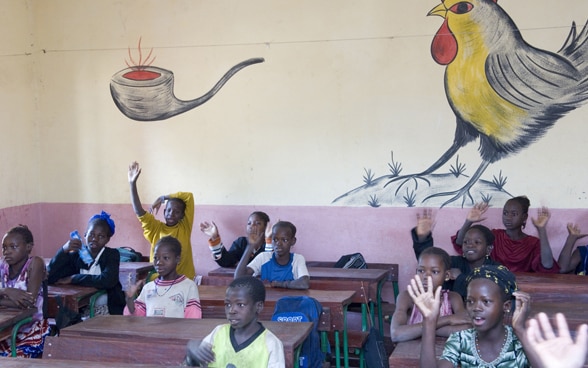 Clase escolar en Malí frente a una pared pintada con colores vivos.