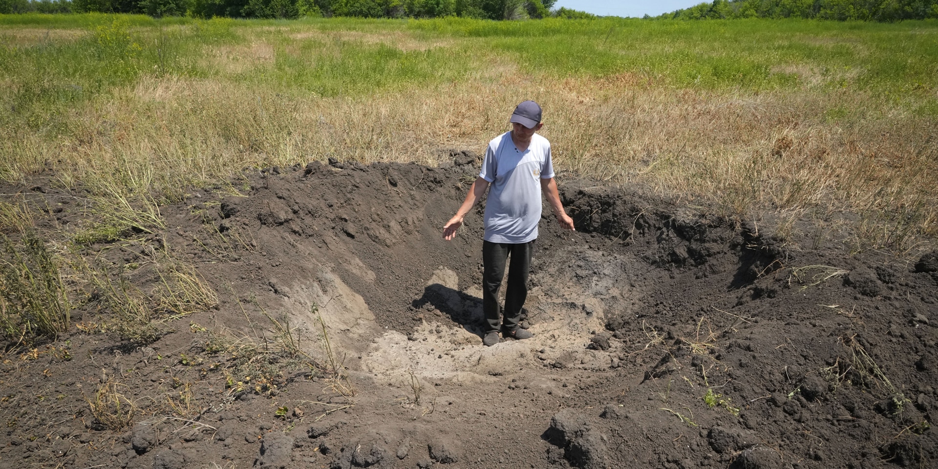 Un agriculteur ukrainien montre la cratère laissé par un obus russe dans son champs.