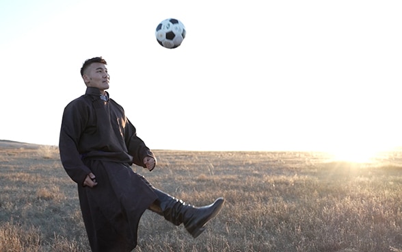 Un homme tape dans un ballon. En arrière-plan se dessine la steppe mongole.