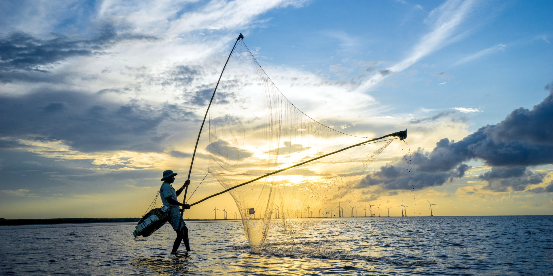 Ein Fischer steht bei Sonnenaufgang mit seinem Netz im Mekong.