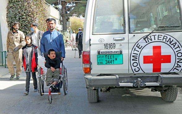 Visitantes de un hospital afgano pasan junto a un vehículo del CICR.