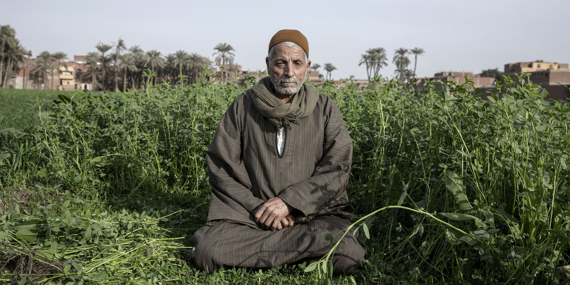 Un contadino del governatorato di Assuan seduto a gambe incrociate nel suo campo vicino alla grande  diga.