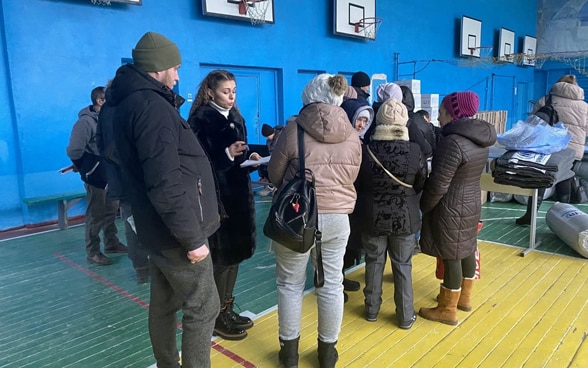 A woman talks to people arriving in a gymnasium that has been converted into an emergency shelter. 