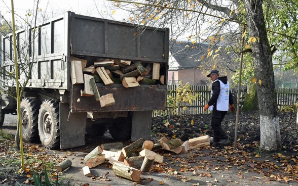 Ein Mann steht neben einem Lastwagen, der Holz ablädt.