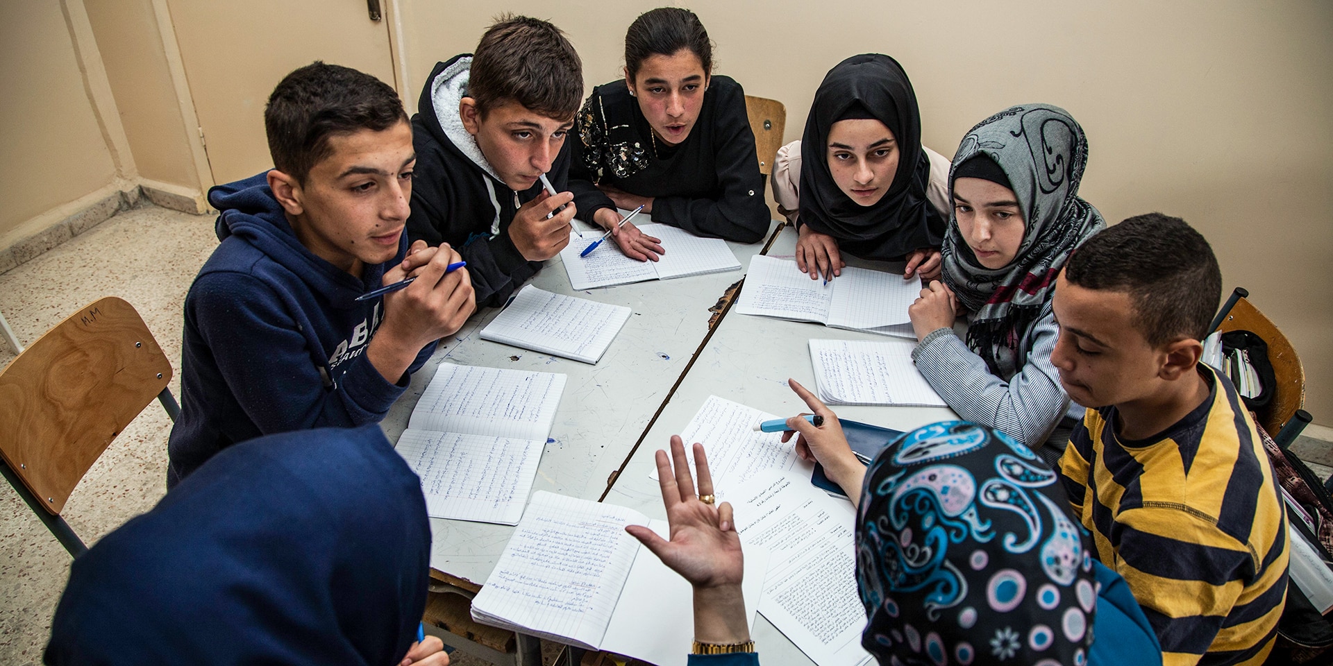 Un gruppo di giovani è seduto attorno a un tavolo. Insieme fanno risolvono dei compiti scolastici. 