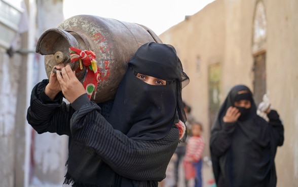 Deux femmes portent une bouteille de gaz sur l'épaule et partent à la recherche de gaz sur le marché noir.