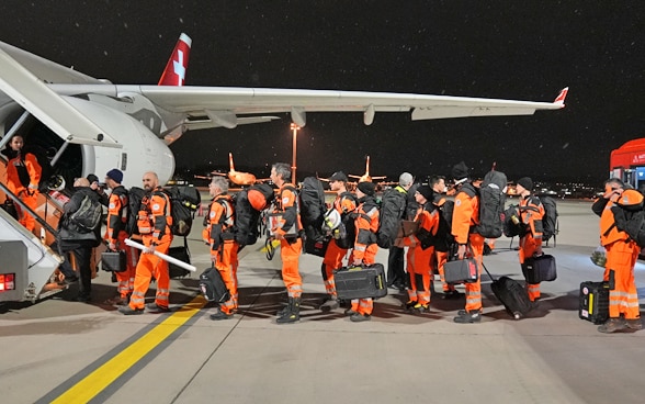 Una decina di membri della Catena svizzera di salvataggio in fila davanti alla scaletta dell’aereo.