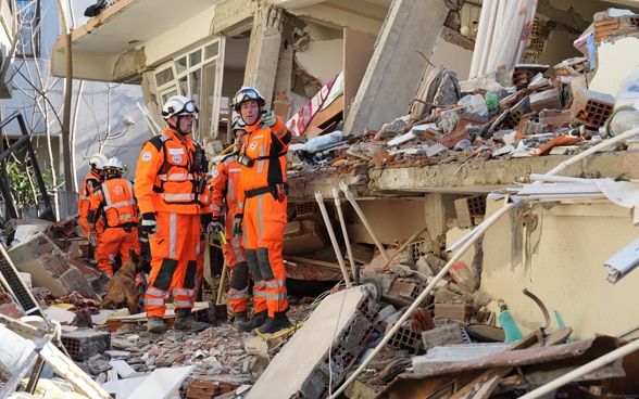  Deux membres de la Chaîne suisse de sauvetage se tiennent devant un bâtiment dont le mur extérieur est détruit.