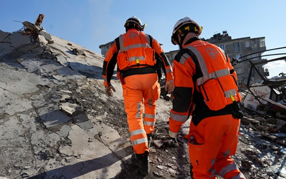  Deux membres de la Chaîne suisse de sauvetage marchent sur le mur d'une maison qui s'est effondrée.