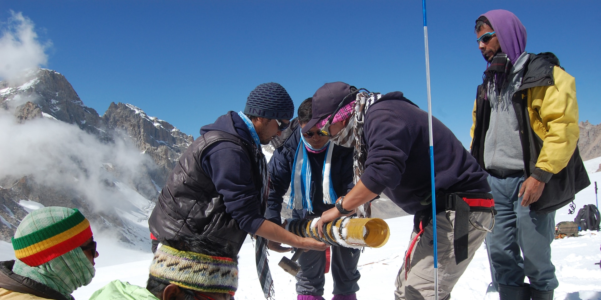 Sept hommes effectuent des mesures scientifiques dans la neige sur un glacier au cœur des montagnes.