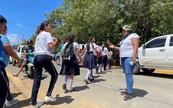 A woman guides a group of pupils across the road.