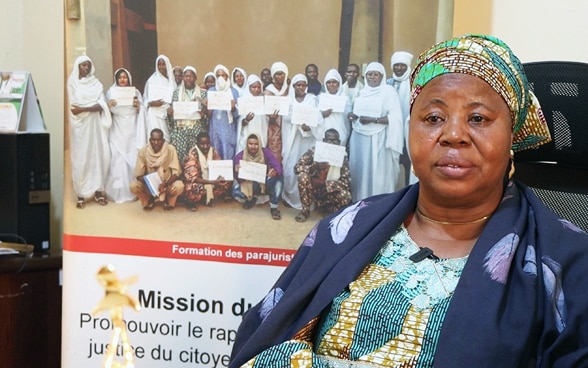 La directrice exécutive de WILDAF Mali est assise sur une chaise de bureau. Sur le fond, il y a une affiche avec des femmes artisans de paix