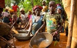 Frauen, Männer und Kinder aus einem Dorf in Sierra Leone, die hüfttief im Wasser stehen und versuchen, das geschürfte Gold von Verunreinigungen zu befreien.