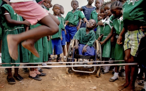 Un grupo de alumnos nigerianos juegan a la comba. Entre ellos, un niño con discapacidad motriz sonríe sentado en una silla de ruedas.