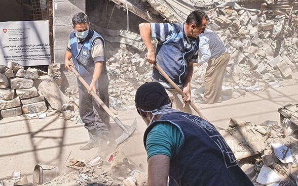 En Syrie, trois hommes déblaient des pierres et des gravats.