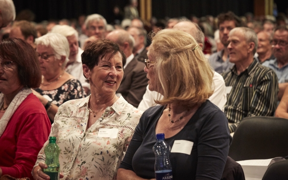 Zwei Teilnehmerinnen sitzen im Publikum der Jahreskonferenz und sprechen angeregt miteinander.