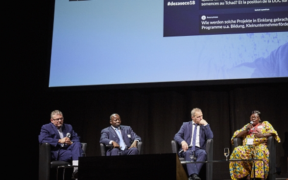 Mansour N’Diaye, Dominique Guenat, Pierre-André Page, Mariane Nguerassem and moderator Melanie Pfändler sitting on stage. In the background is a screen with a presentation of questions from the audience.
