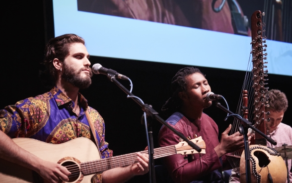 The three musicians with their instruments on stage, sitting in front of microphones.