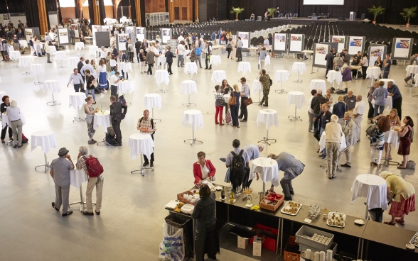 A bird's-eye view of the Bernexpo Festhalle where participants are talking, eating and drinking around a number of standing tables.