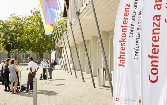 Die Festhalle der Bernexpo von aussen. Es hängen farbige Fahnen vor den Türen und auf weissen Plakaten kann man in verschiedenen Landessprachen und in Englisch lesen: «Jahreskonferenz»