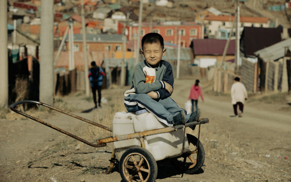 Un garçon aux yeux fermés est assis sur une charrette à bras.
