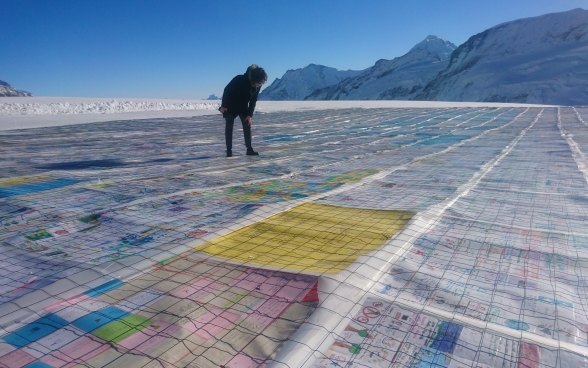 A woman stands on a glacier and looks down at some of the postcards.