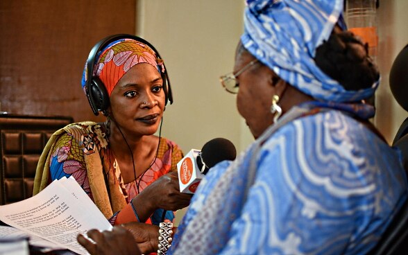 Eine afrikanische Frau interviewt mit einem Mikrofon in einem Radiostudio eine andere Frau.