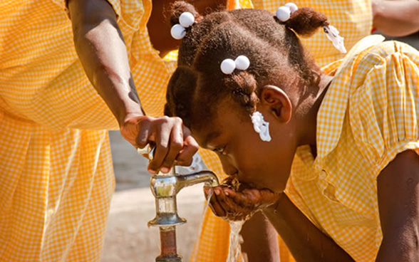 Una niña bebe agua de un grifo