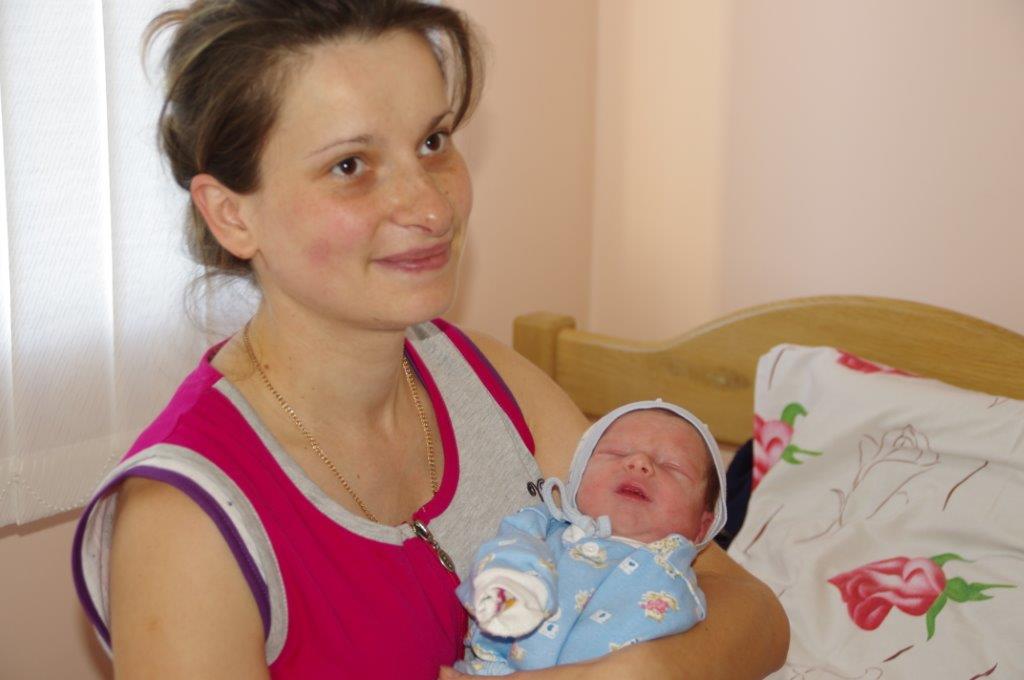Eine Mutter hält ihr Neugeborenes lächelnd auf dem Arm.