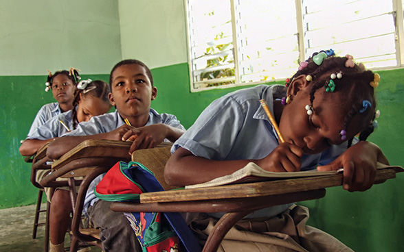 Drei Mädchen und ein Junge sitzen in einem Klassenzimmer.